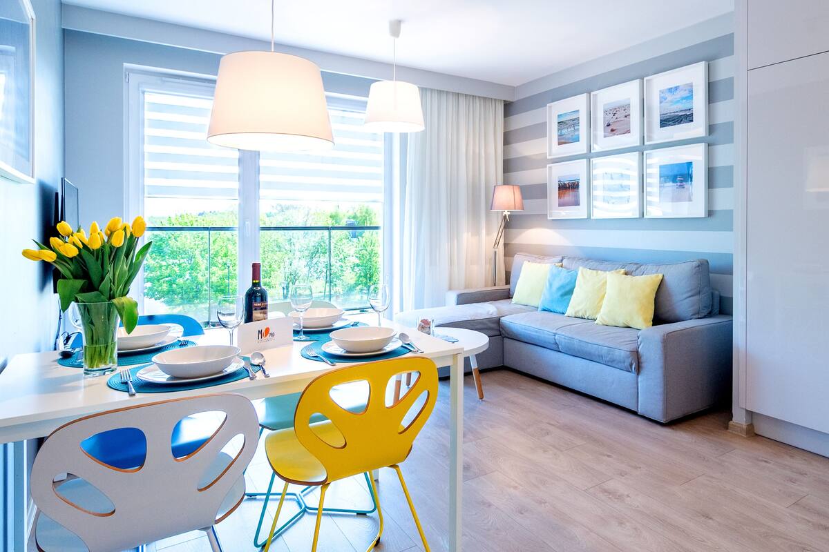 Une cuisine moderne avec un coin repas, comprenant un canapé gris, des chaises jaunes et une table à manger pour quatre personnes.