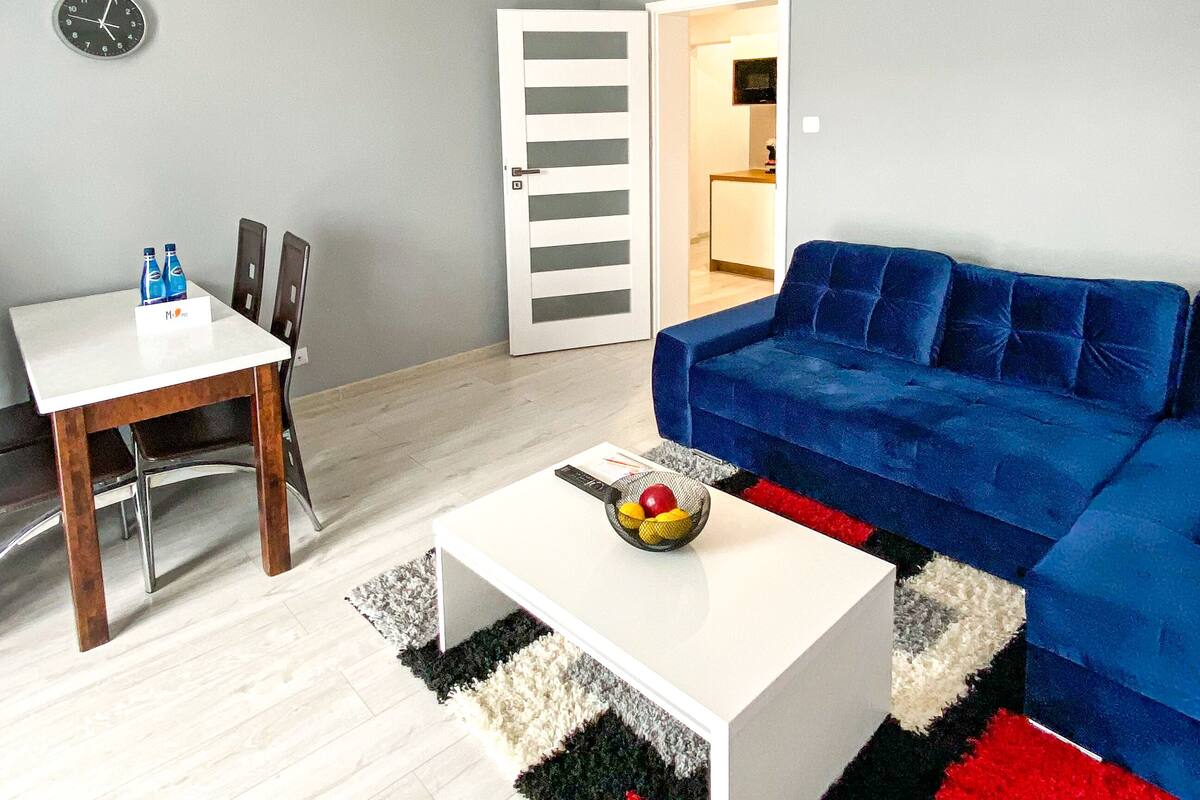 Un salon moderne avec une table basse blanche, un canapé bleu et un coin repas comprenant une table et des chaises blanches.