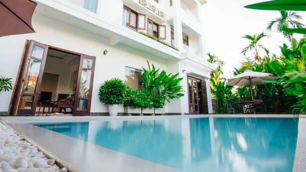 Un hotel moderno con piscina, mobiliario exterior y exuberante vegetación.