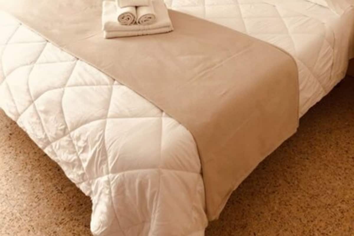 Una cama bien tendida con una colcha acolchada, una toalla doblada y un cabecero de madera.