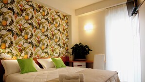 Habitació d'hotel amb llit, almoines, una tauleta de nit, una planta i una paret amb dibuix de fruita.