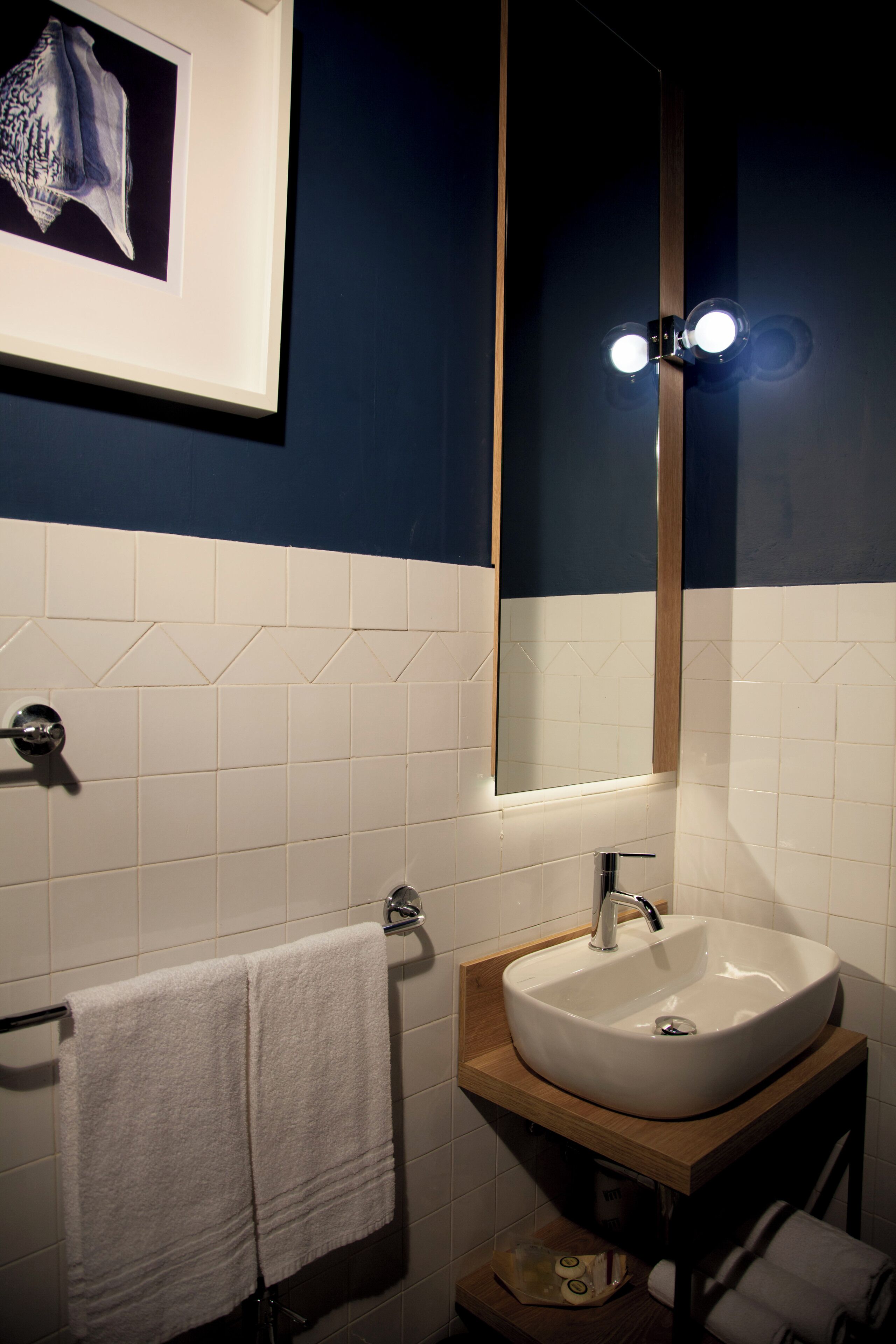 A bathroom with a white sink, a mirror, and a framed picture on the wall.