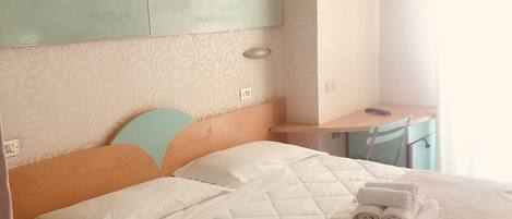 Una cama bien tendida con un edredón blanco acolchado, un cabecero de madera y una mesita de noche con una lámpara.