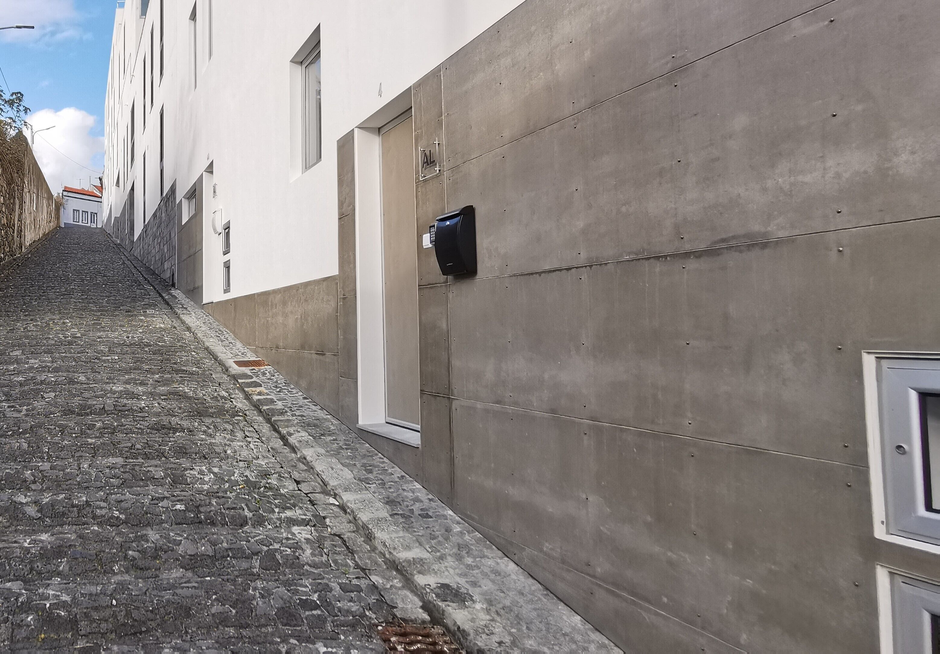 Una calle empedrada y estrecha bordeada por edificios de fachada de hormigón y una puerta con la inscripción 