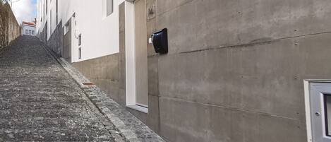 A narrow cobblestone street flanked by buildings with a concrete facade and a door marked "TAL".