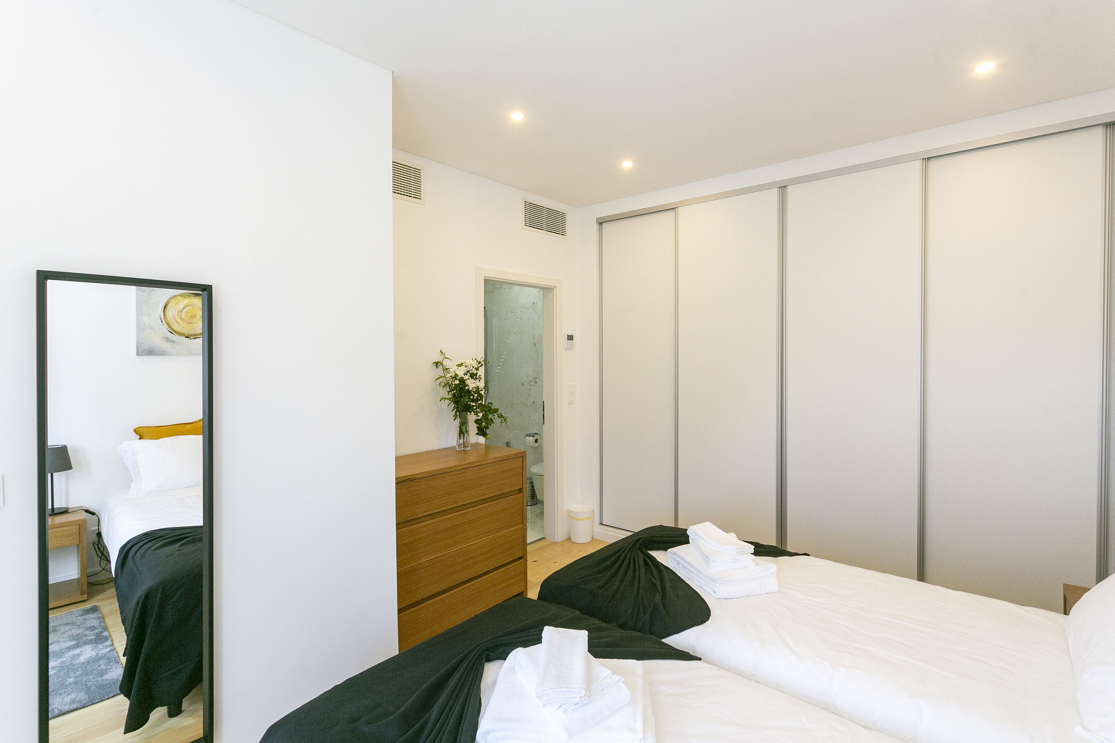 A modern bedroom with a large bed, a dresser, a mirror, and a walk-in closet.