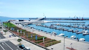 A marina with boats docked, a road with cars, and a building with a sloped roof. - Home Azores – Casas da Ladeira (Ponta Delgada)