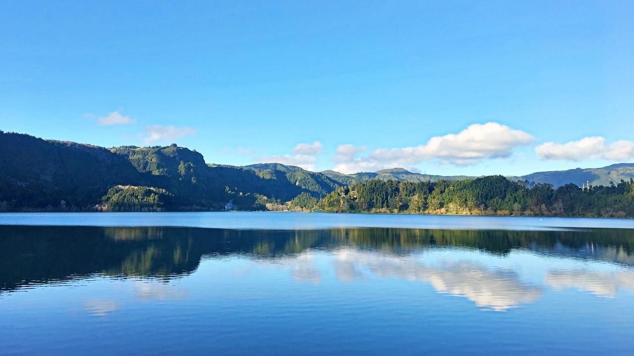 A calm lake with reflections of the surrounding hills and a clear sky.
