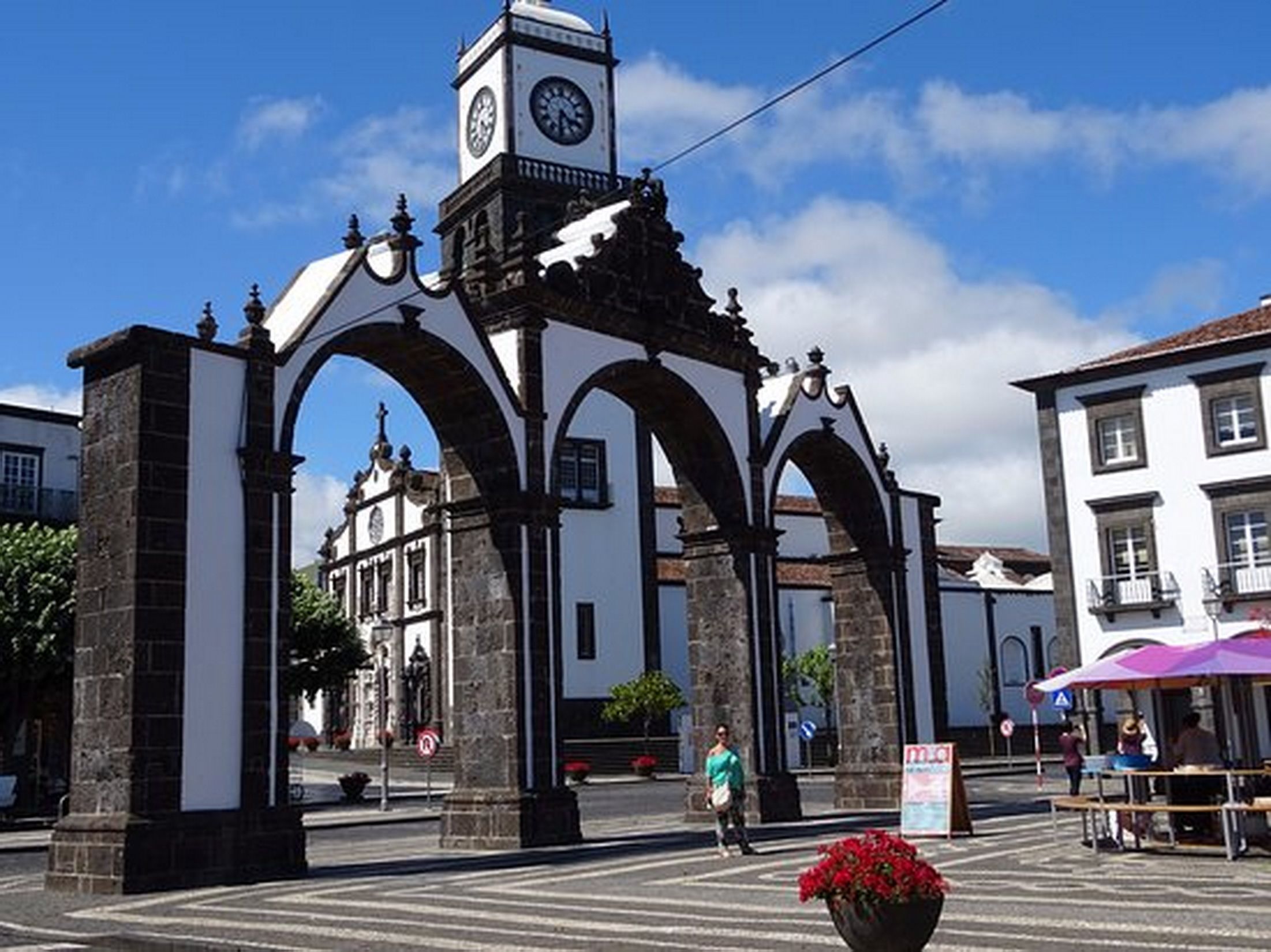 Un edificio histórico con una torre de reloj, arcos y una calle con gente caminando.