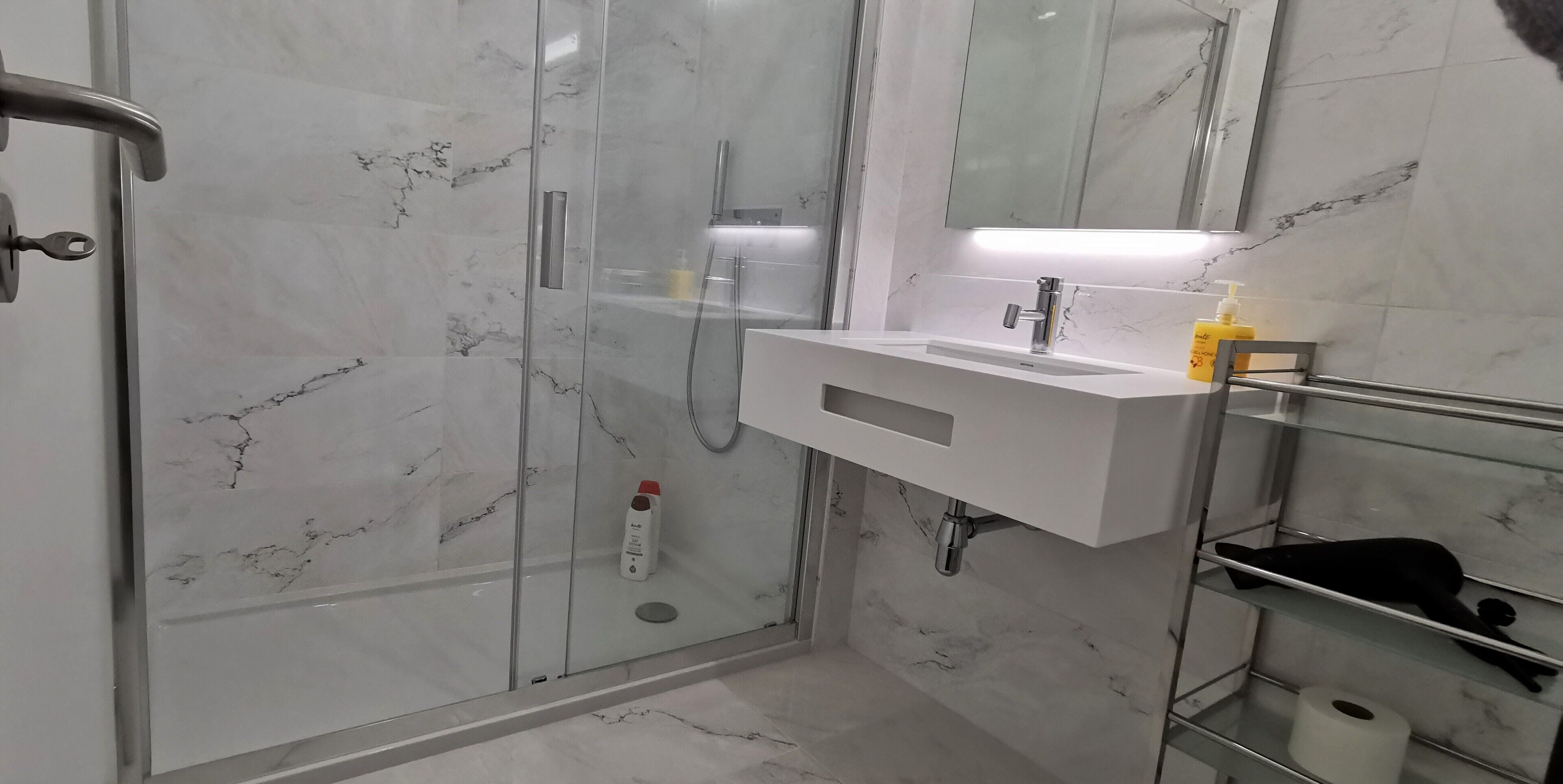 Ein modernes Badezimmer mit einer Duschkabine aus Glas, einem weißen Waschbecken mit Spiegel darüber und einem Ablagebereich für Toilettenartikel.