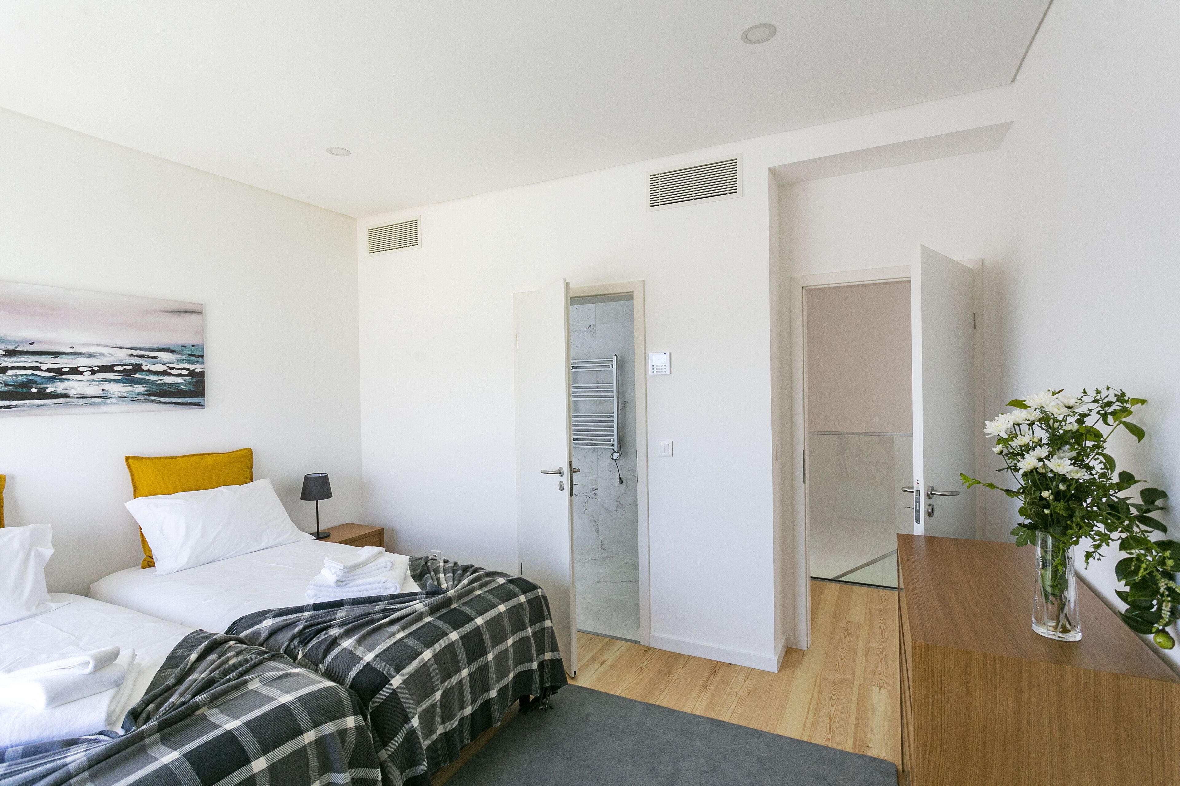 Un dormitorio moderno con cama, mesita de noche, espejo, puerta y una planta pequeña.