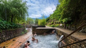 A natural hot spring area with stone walls and wooden walkways, surrounded by lush greenery. - Home Azores – Casas da Ladeira (Ponta Delgada)
