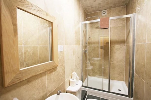 Et badeværelse med en brusekabine med glasvægge, et spejl med træramme og et toilet med toiletpapir.