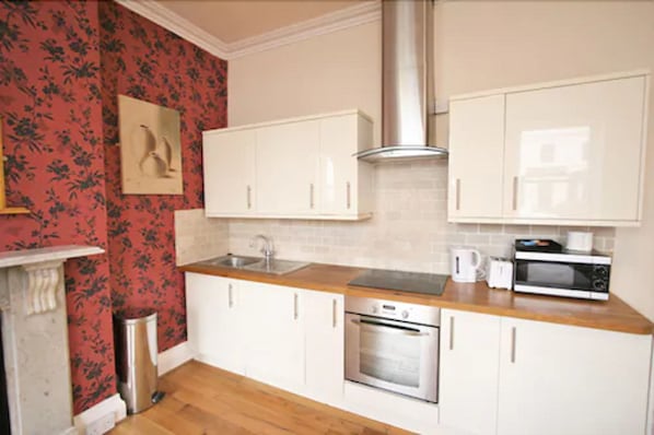 A kitchen with white cabinets, a stainless steel range hood, a microwave, and a sink. - Central Studios Gloucester Place (Cheltenham)