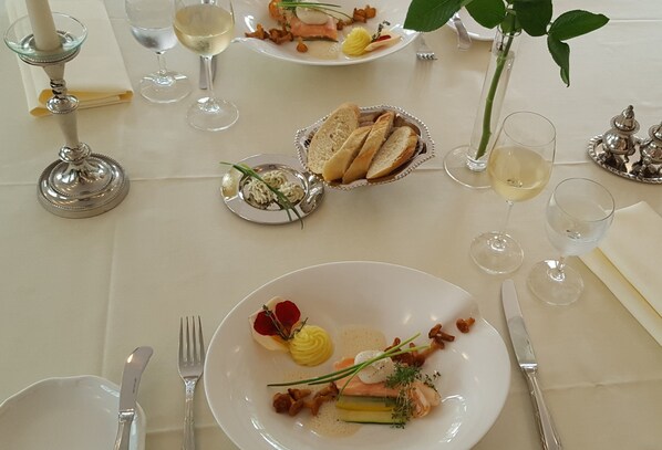 Una mesa de comedor dispuesta con platos de comida, copas de vino y cubiertos.