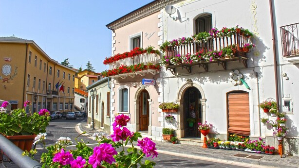 A building with a balcony adorned with flowers, a sign indicating a beauty salon, and a door with a shutter. - La Maison (Vallata)