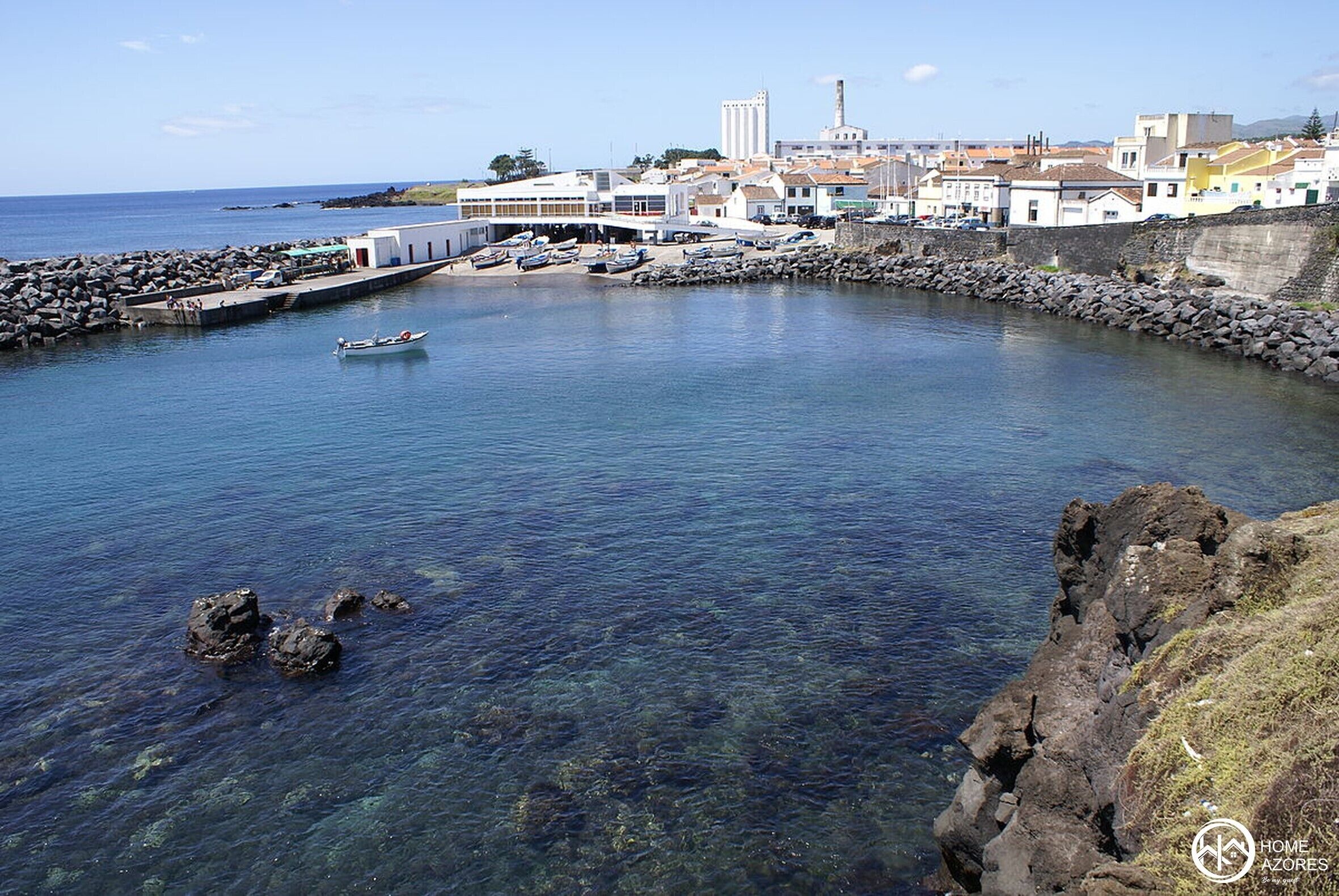 A coastal town with a clear harbor, rocky shoreline, and buildings in the background.