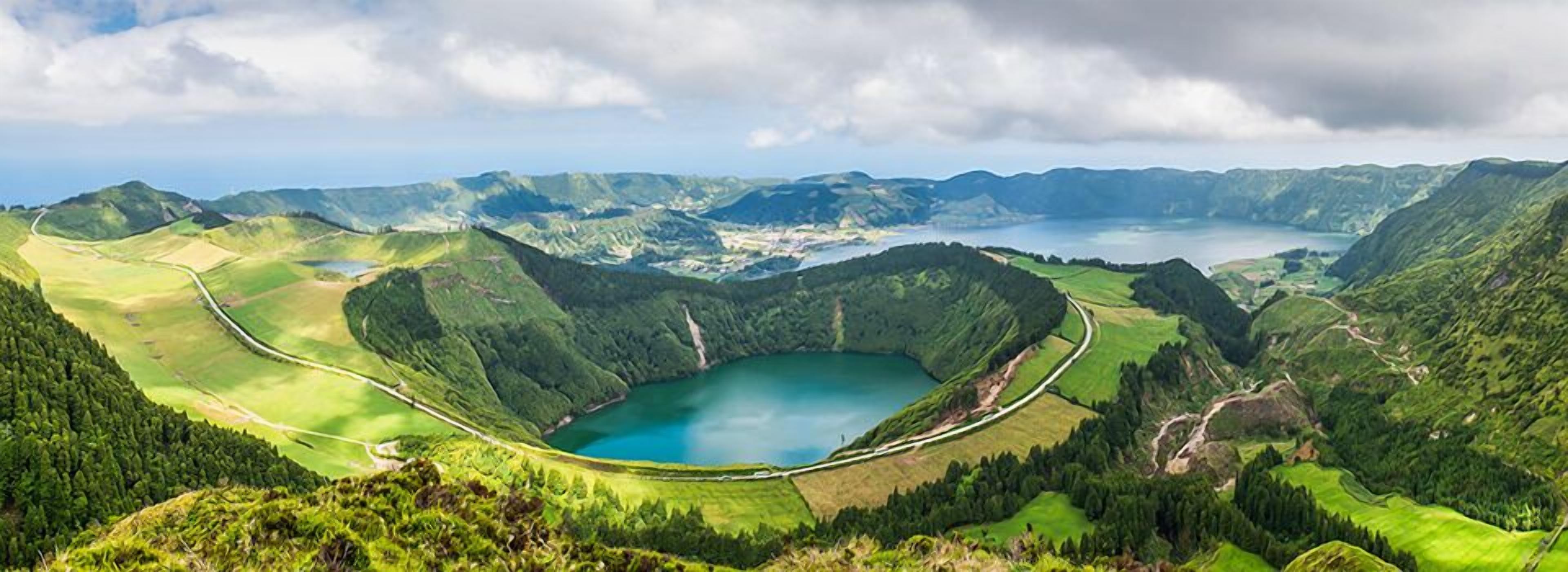 Una vista panorámica de un valle con un lago, rodeado de colinas verdes y una carretera sinuosa.