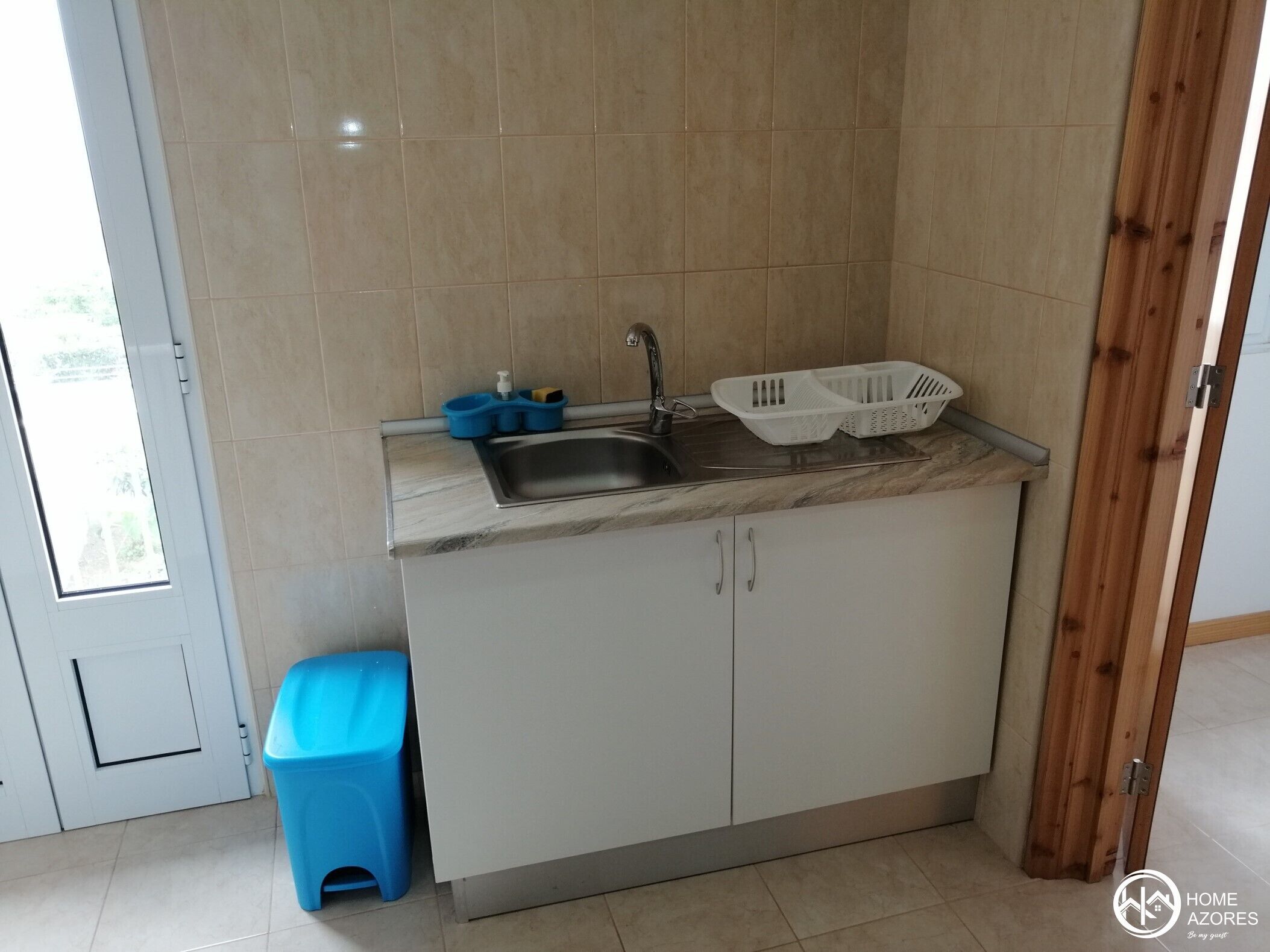 A kitchen with a sink, a blue stool, and two white baskets on the counter.