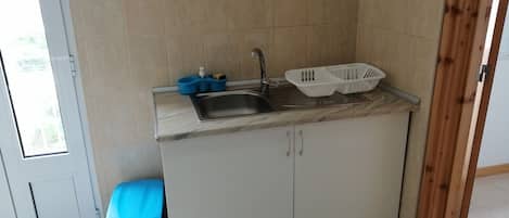 A kitchen with a sink, a blue stool, and two white baskets on the counter.