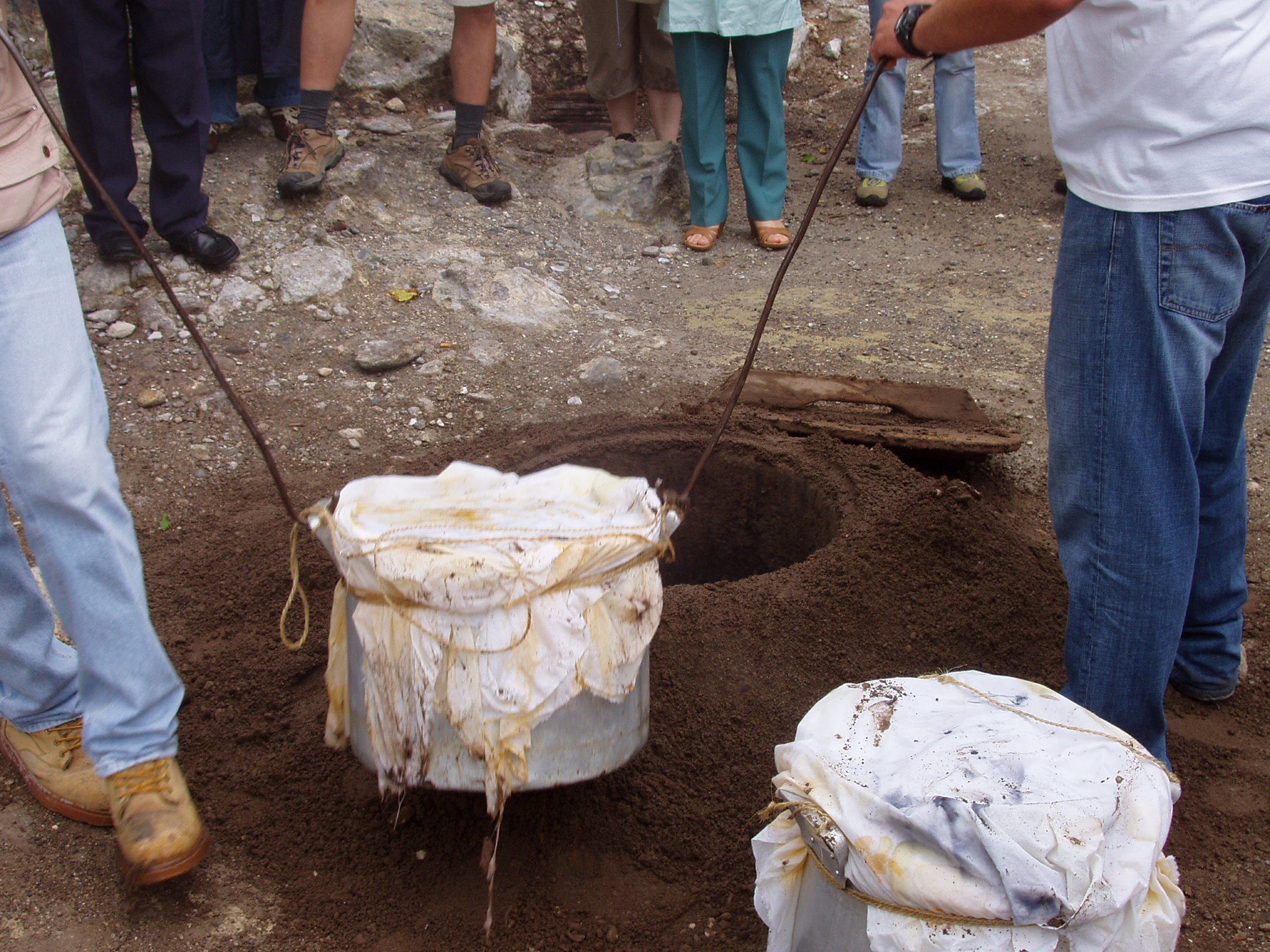 A group of people engaged in an excavation activity, using shovels and a large white sack to dig a hole in the ground.
