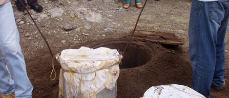 A group of people engaged in an excavation activity, using shovels and a large white sack to dig a hole in the ground.