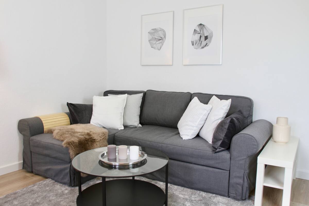 A modern living room with a grey sofa, a round glass coffee table, and a small white side table.