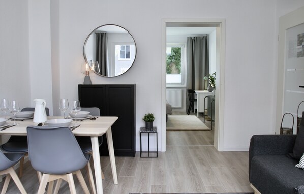A modern dining area with a table set for four, a black cabinet, and a round mirror on the wall. - Apartmenthaus in der Metzstraße (Bochum)