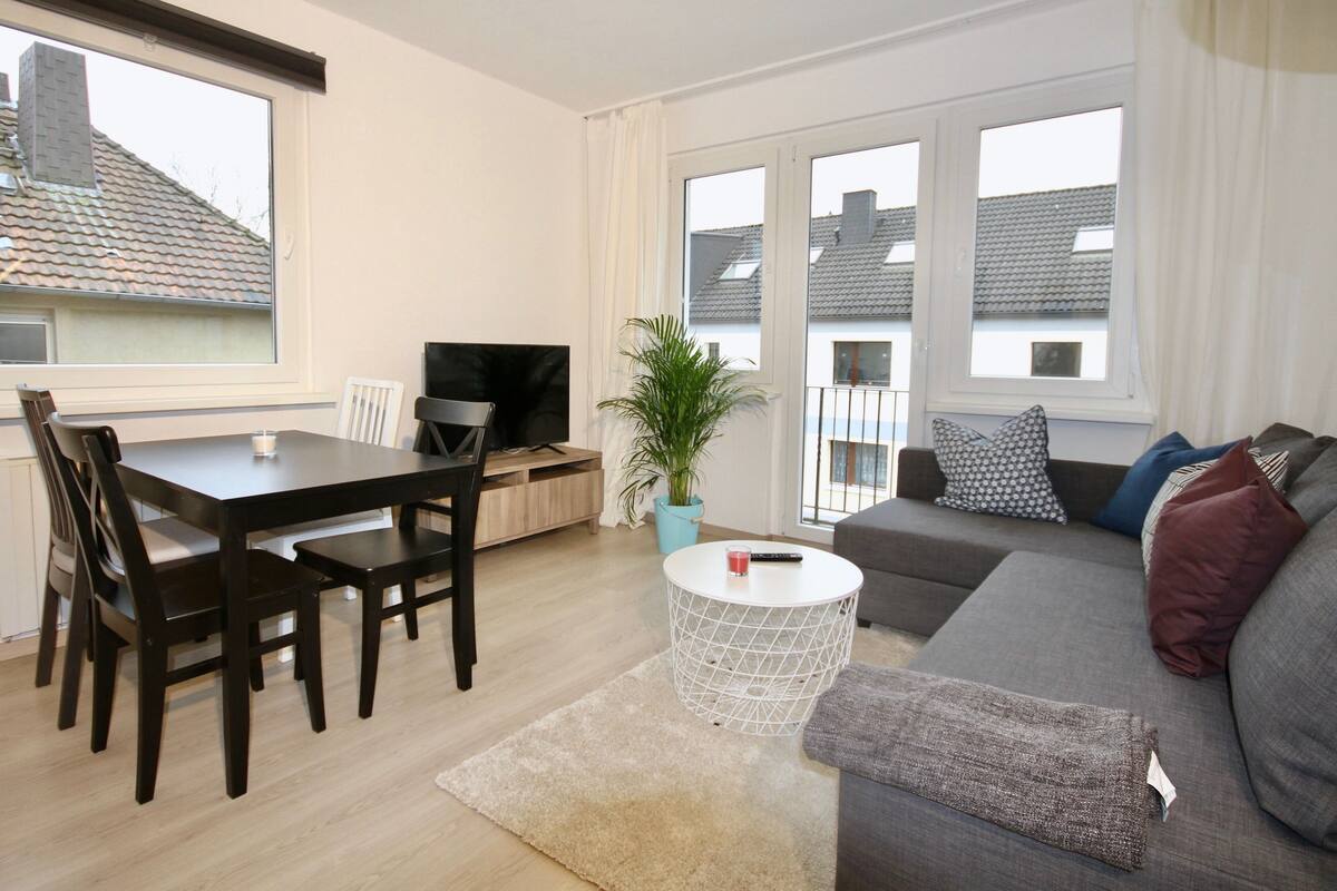 A modern living room with a dining table, chairs, a sofa, and a TV.