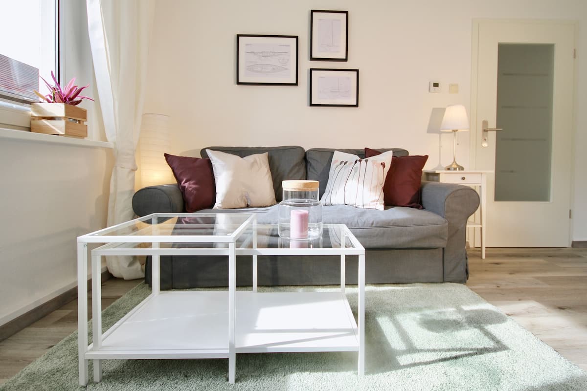A living room with a grey sofa, a white coffee table, and a framed architectural drawing on the wall.