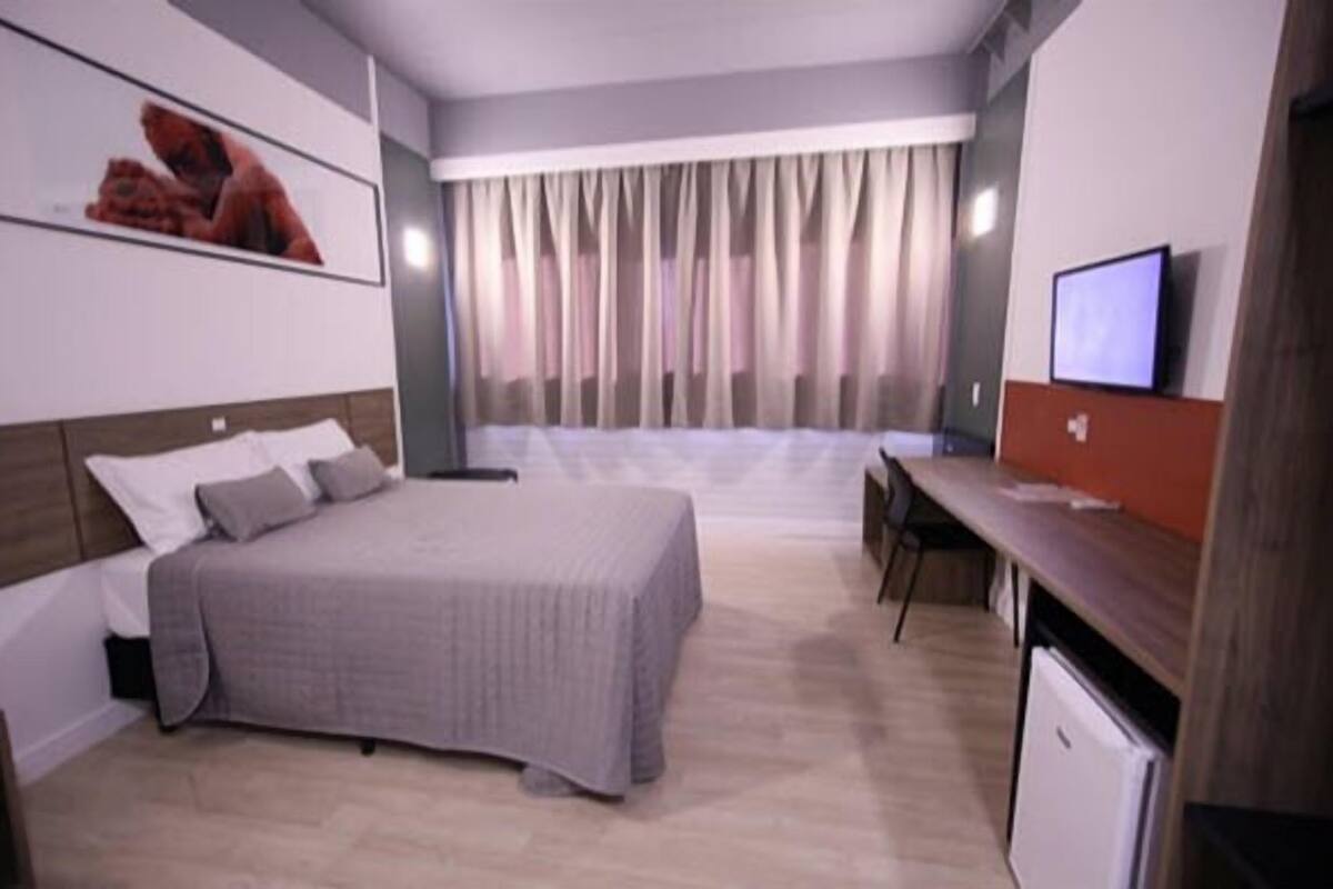Une chambre d’hôtel avec un lit, un bureau, une télévision et une fenêtre avec des rideaux.