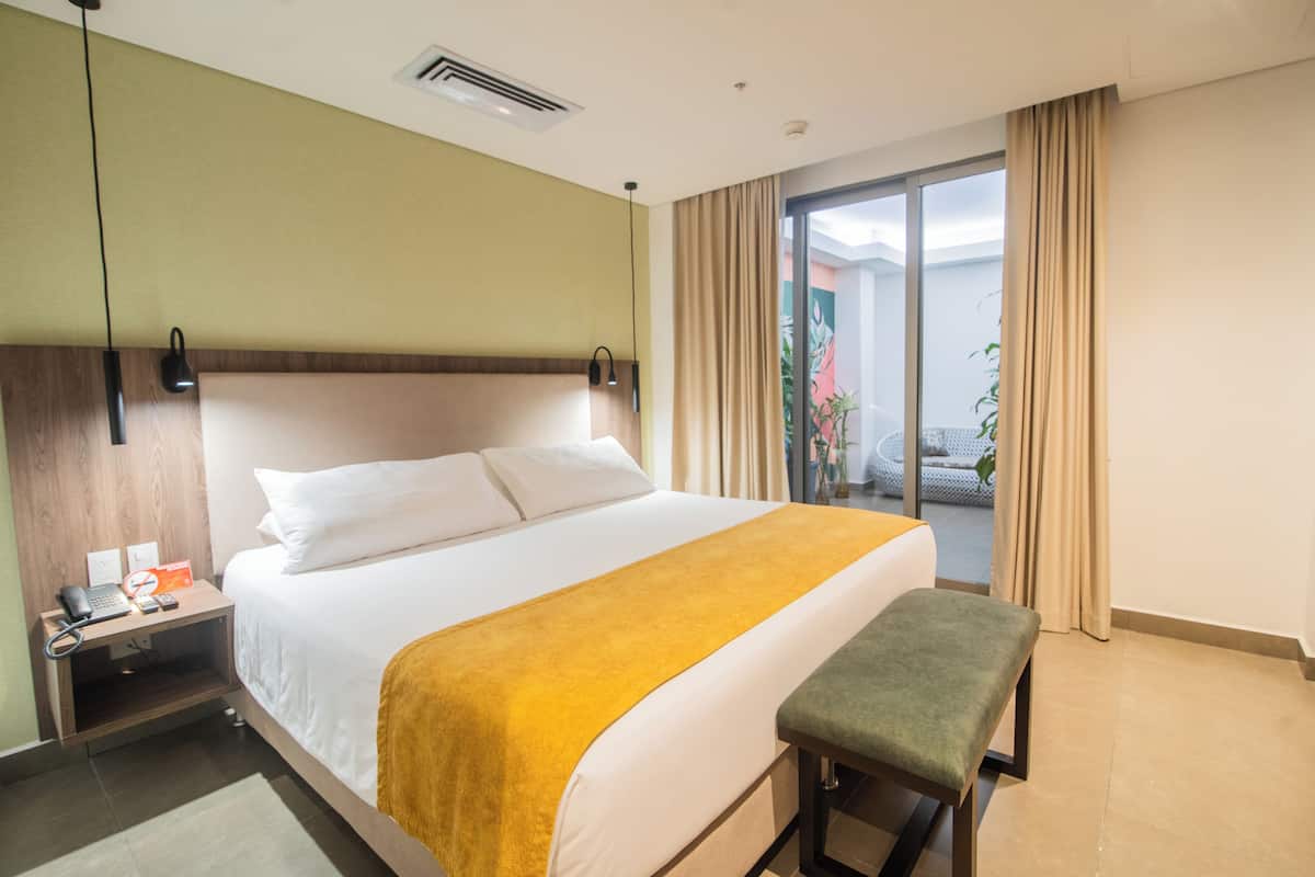 Hotelkamer met een groot bed, een nachtkastje met telefoon en afstandsbediening, een bankje en uitzicht buiten via een schuifdeur.