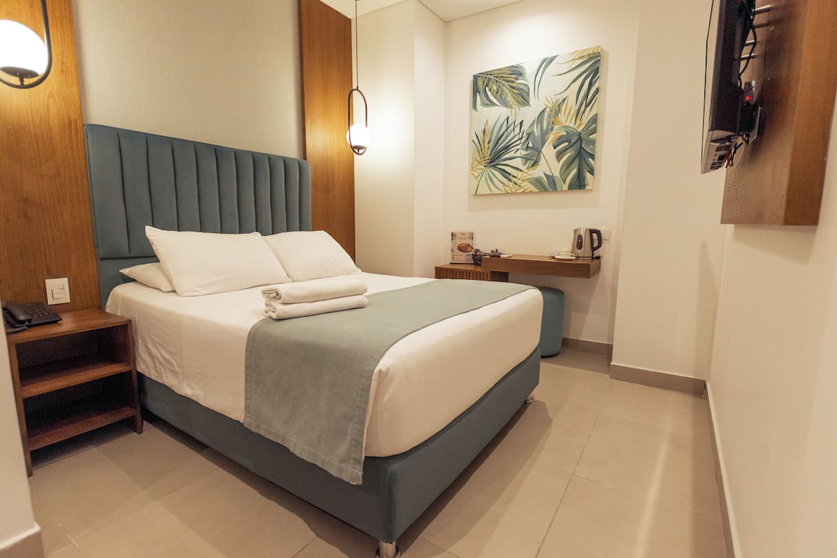 Een moderne hotelkamer met een bed, nachtkastje, lamp, kunstwerk en een wandgemonteerde flatscreen-televisie.