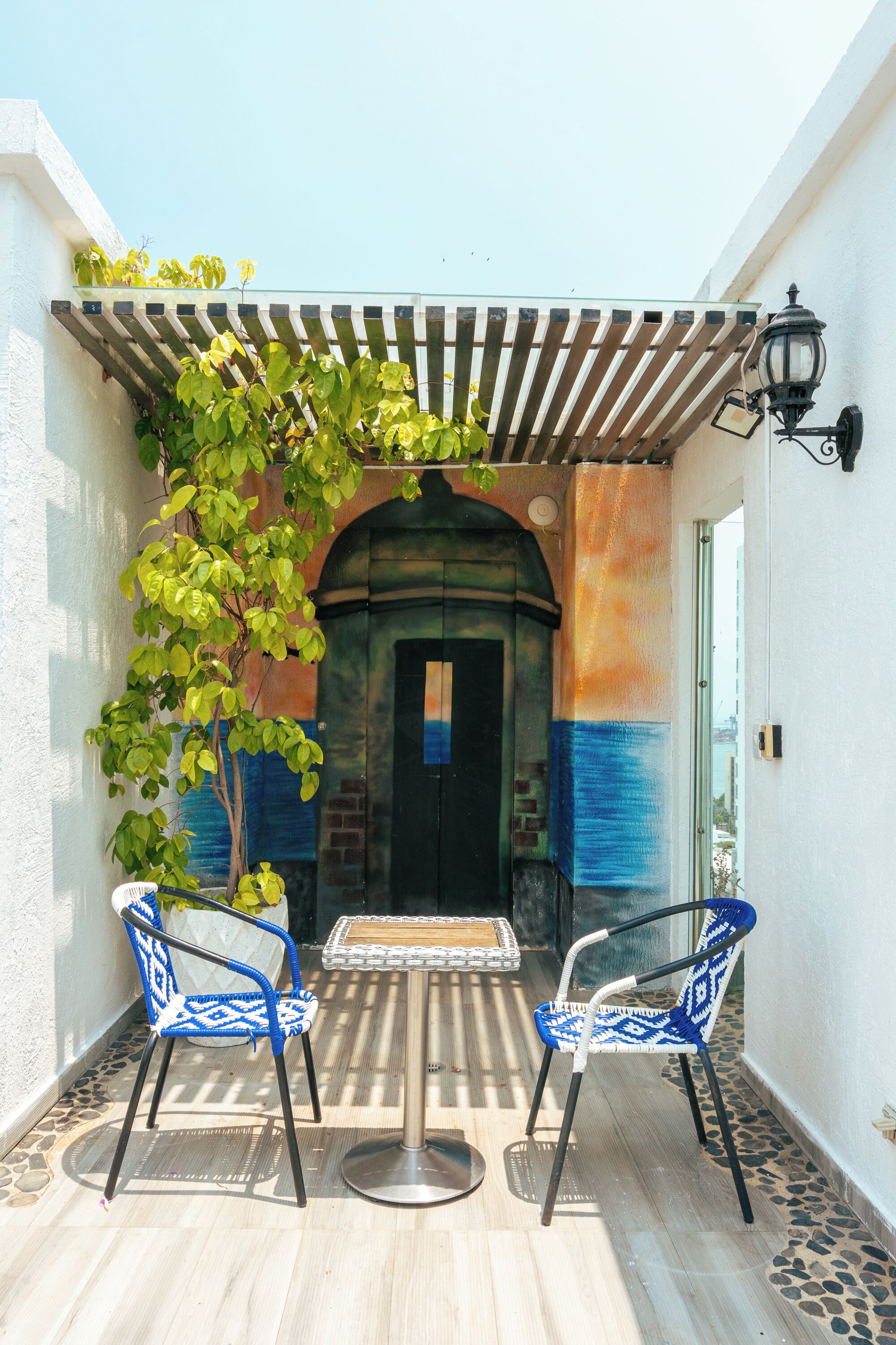 An outdoor patio with two blue patterned chairs, a small table, and a pergola with climbing plants.