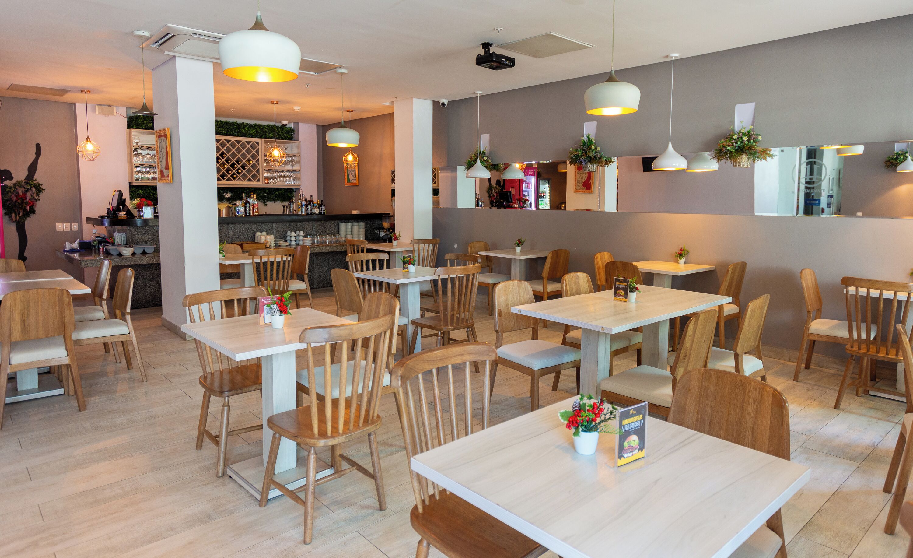 A restaurant interior with wooden tables and chairs, a bar area, and hanging pendant lights.