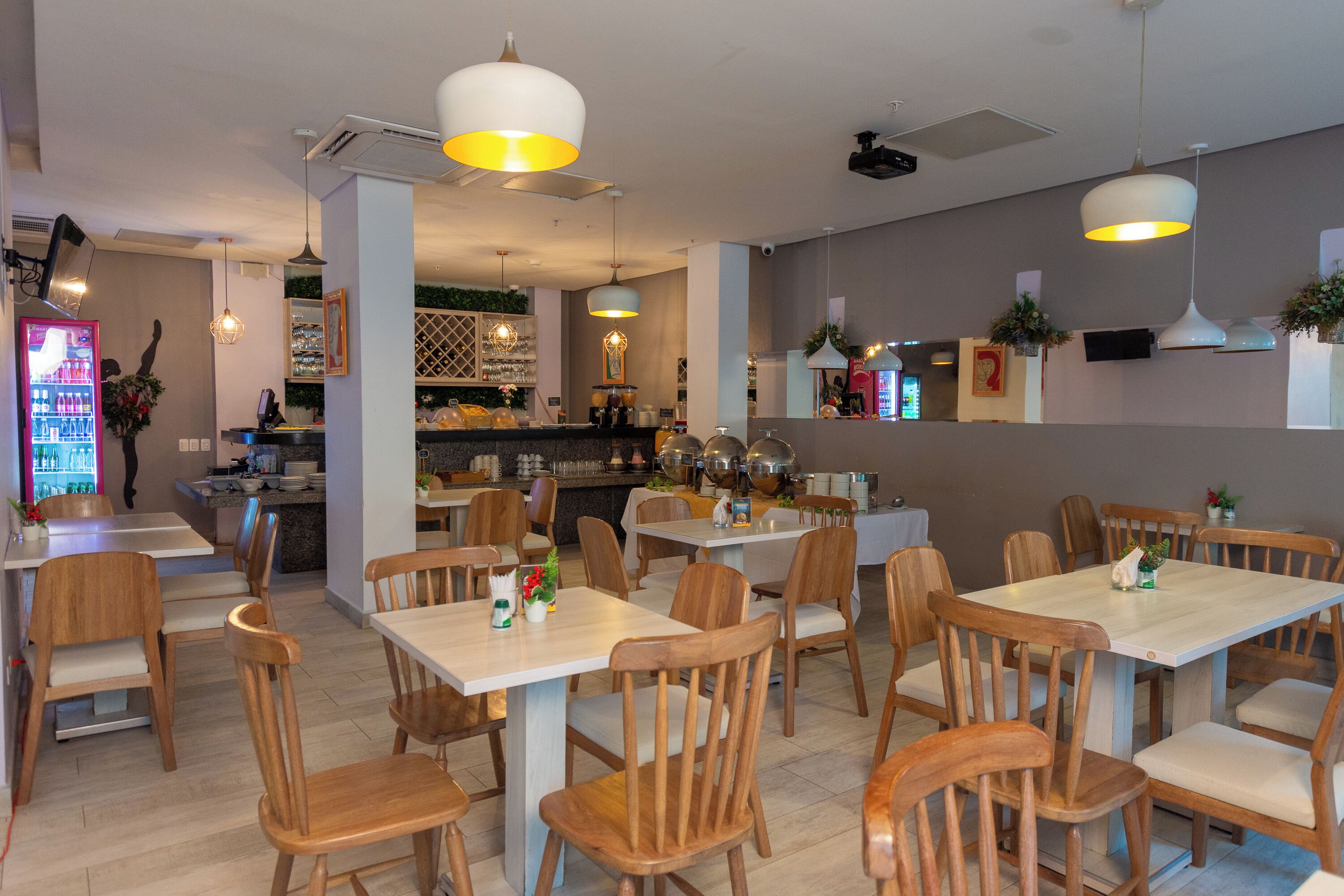 Un restaurant avec des tables et des chaises en bois, des luminaires suspendus et un bar situé au fond de la salle.
