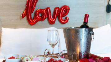 A bed with a decorative wall behind it, a bedside table with a bottle of wine, glasses, and bowls of food.
