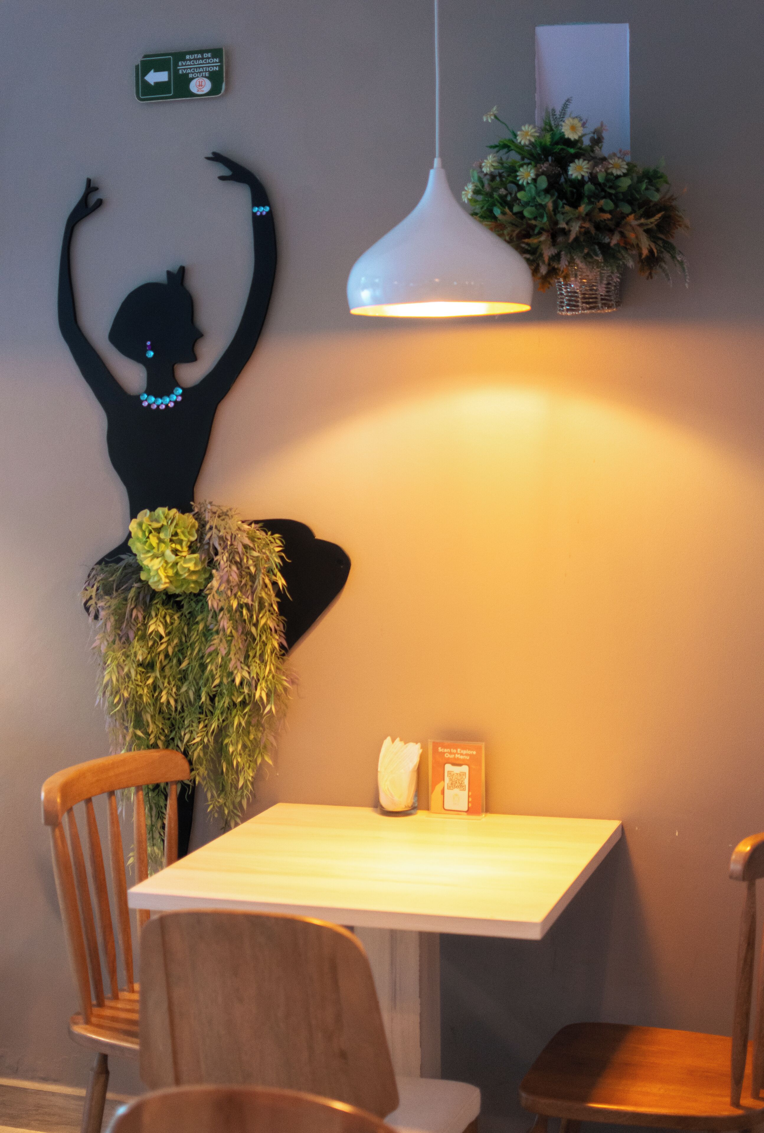 A dining area with a table and chairs, a hanging light fixture, a wall-mounted decoration, and a small plant.