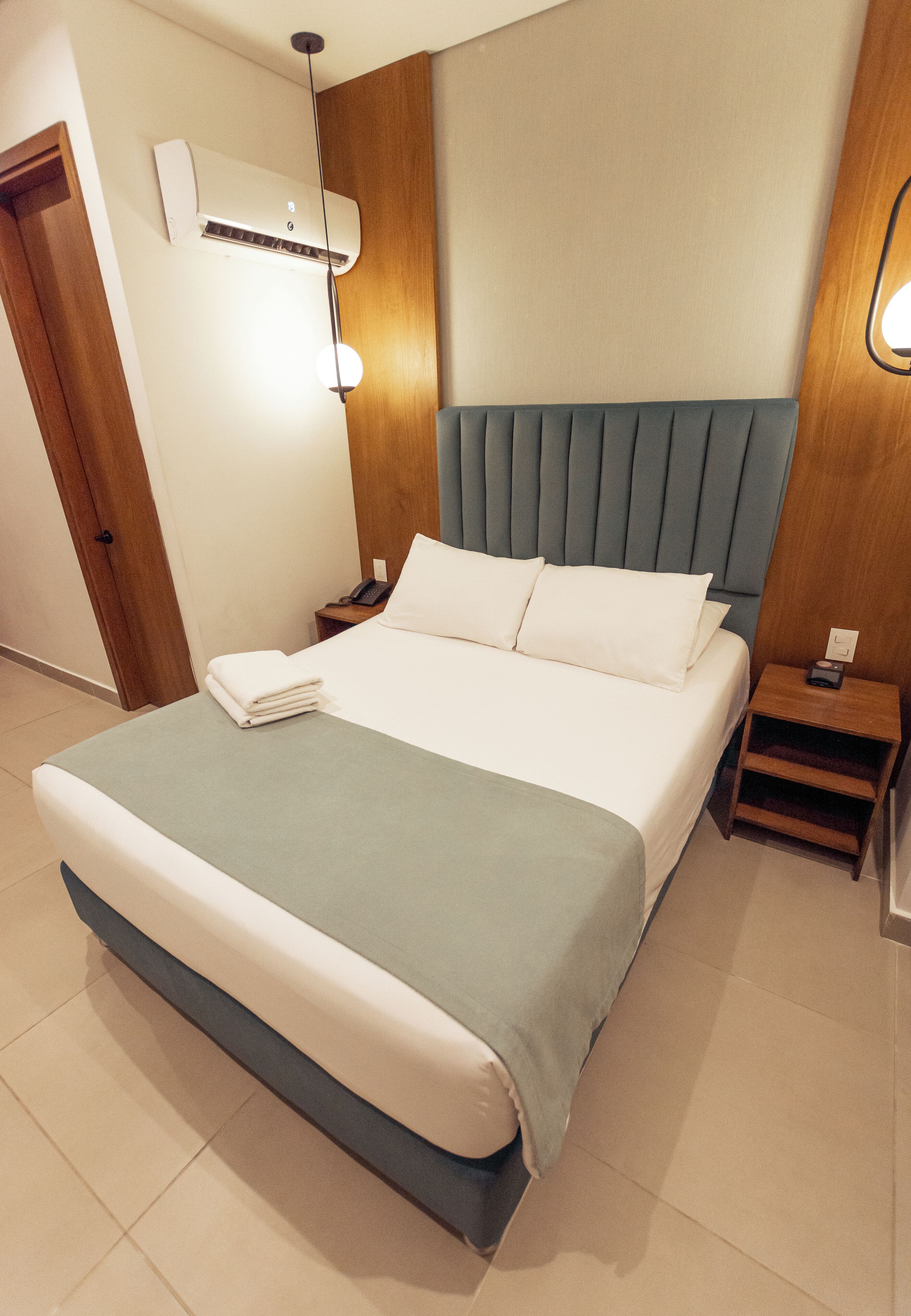 Un hotel moderno con una cama grande, una mesita de noche, un aire acondicionado y una lámpara fijada a la pared.