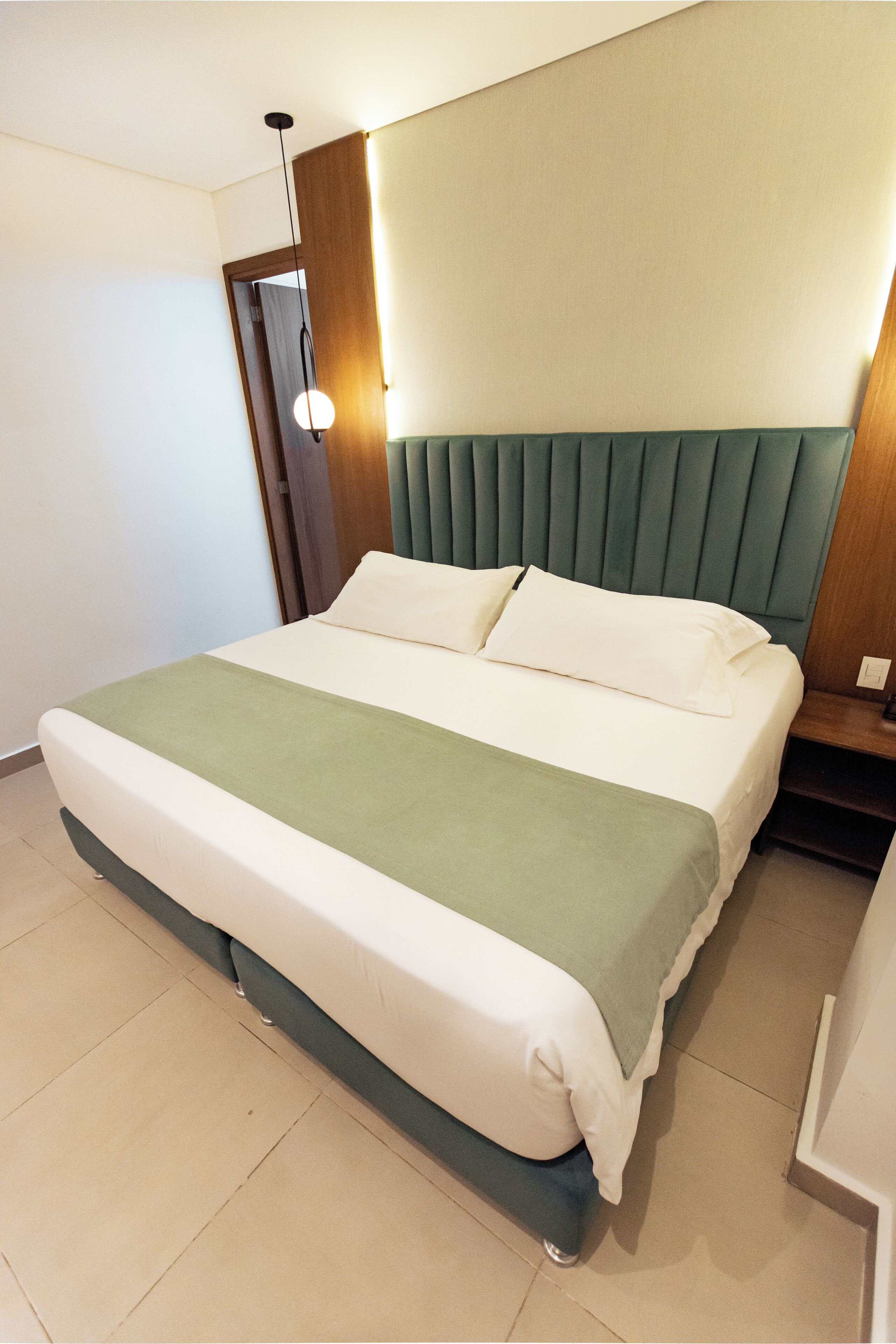 A hotel room with a large bed, a wooden headboard, a bedside table, and a wall-mounted light fixture.