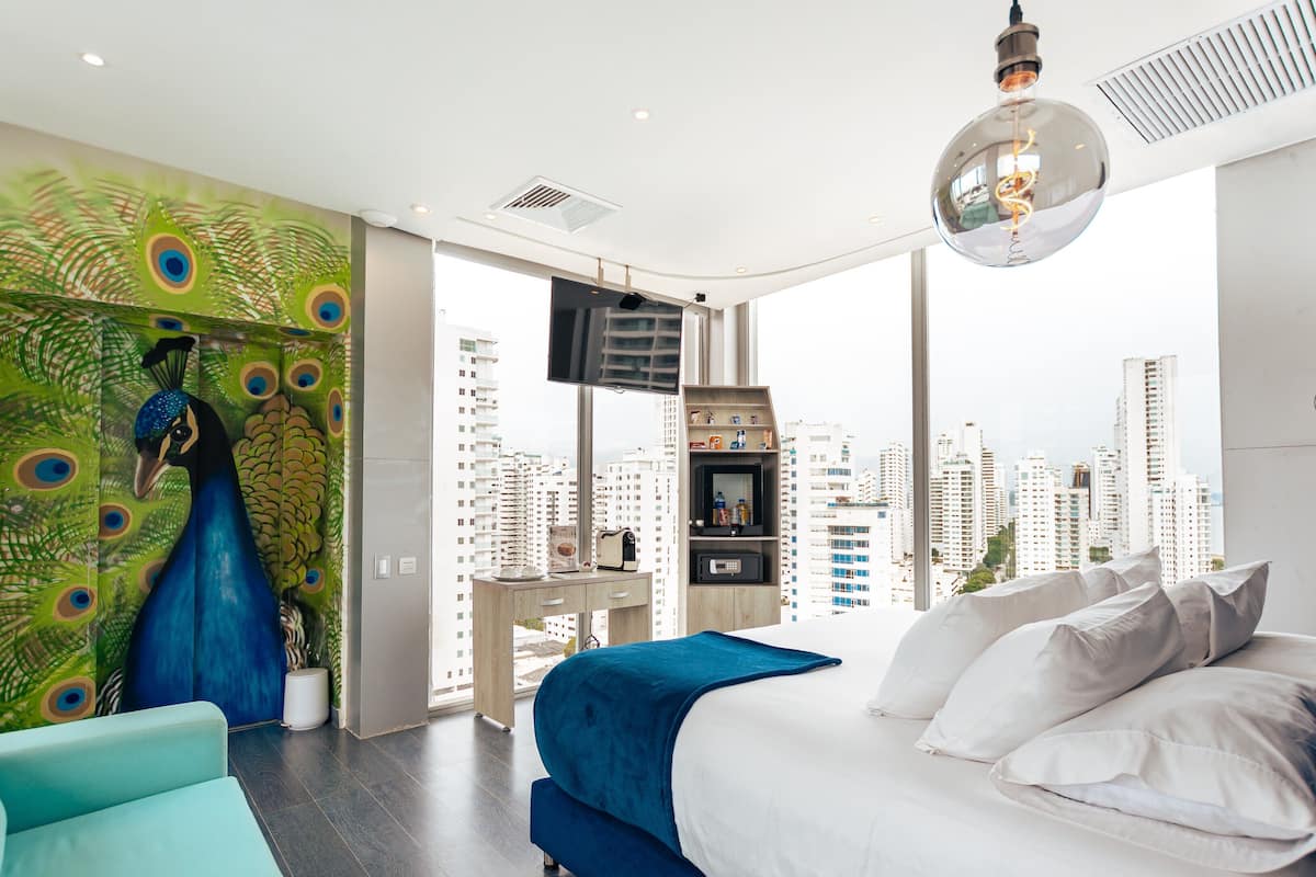 Een moderne slaapkamer met stadszicht, een wand met pauwenmotieven en een groot bed met wit- en blauw beddengoed.