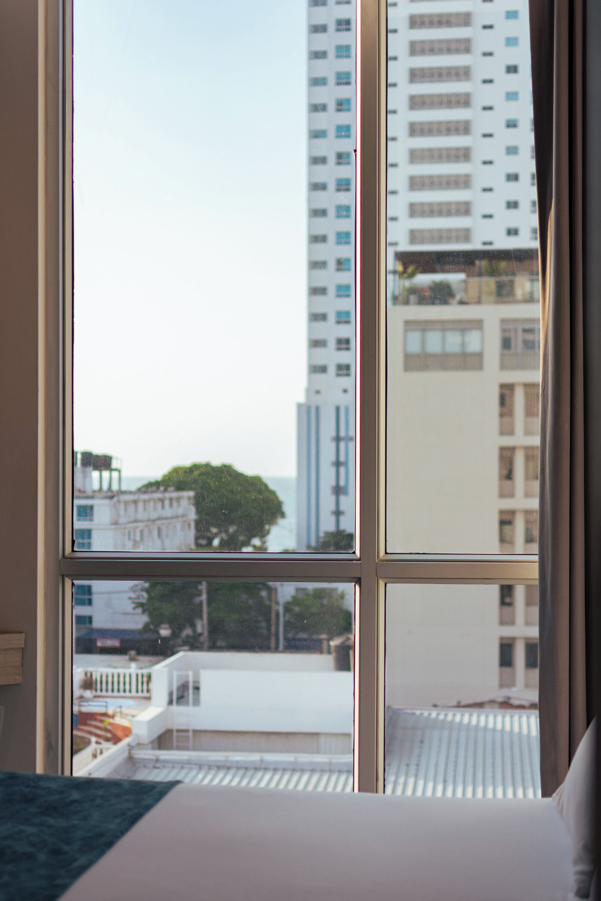 A hotel room with a large window offering a view of tall buildings and a tree.