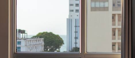 A hotel room with a large window offering a view of tall buildings and a tree.
