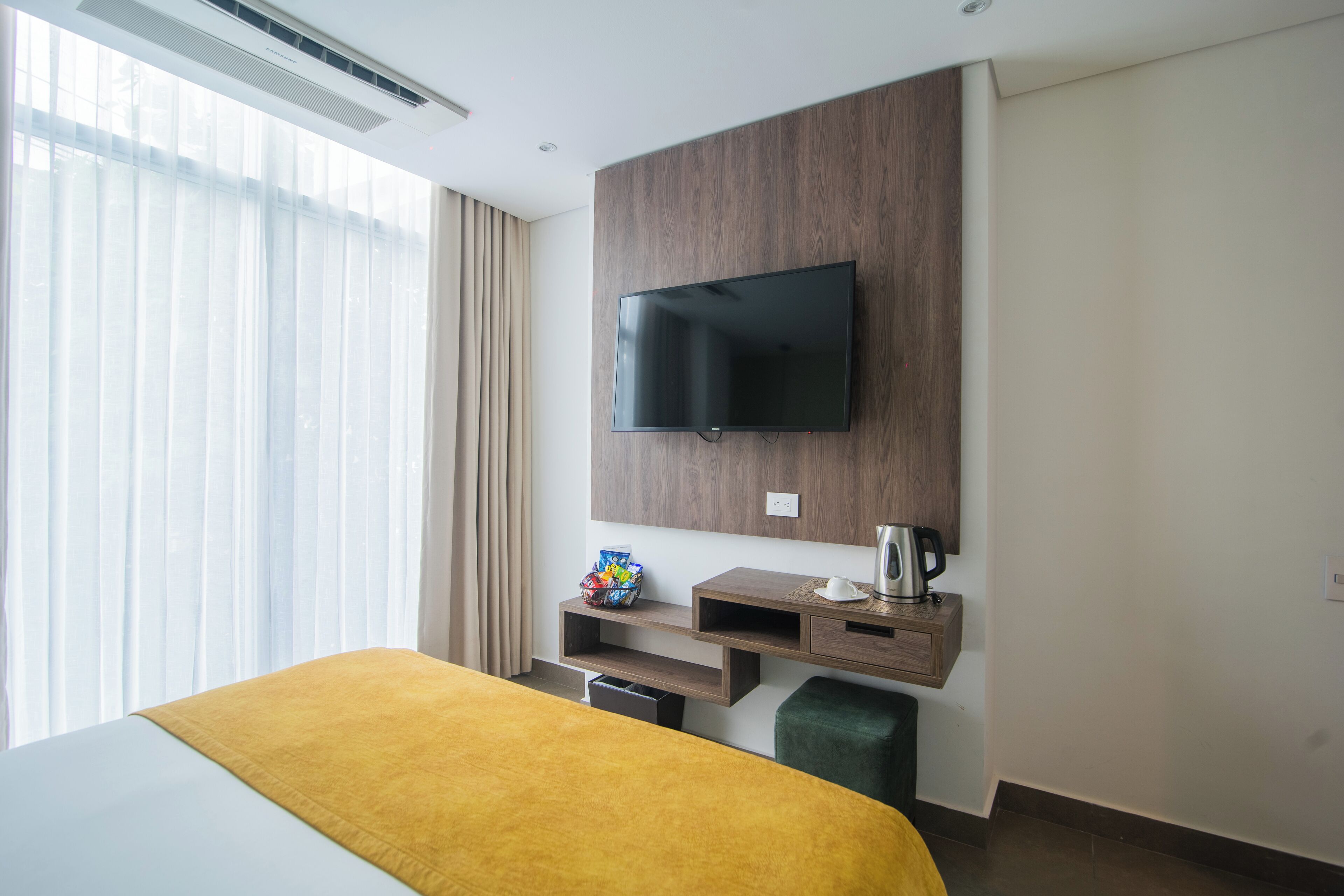 A hotel room with a bed, a mounted TV, a coffee maker, and a small shelf with a decorative item.