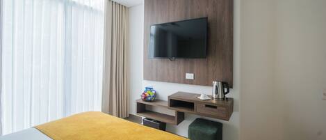 Ein Hotelzimmer mit Bett, einem an der Wand montierten Fernseher, einer Kaffeemaschine und einem kleinen Regal mit einem dekorativen Gegenstand.