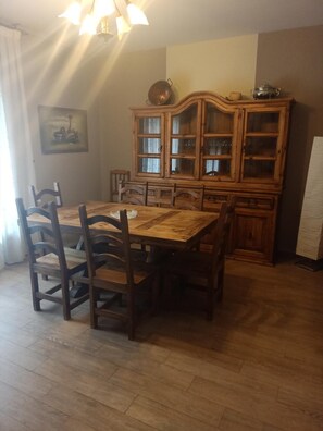 A dining area with a wooden table and chairs, a cabinet with glass doors, and a painting on the wall. - Hostal la Cerca (Arcones)