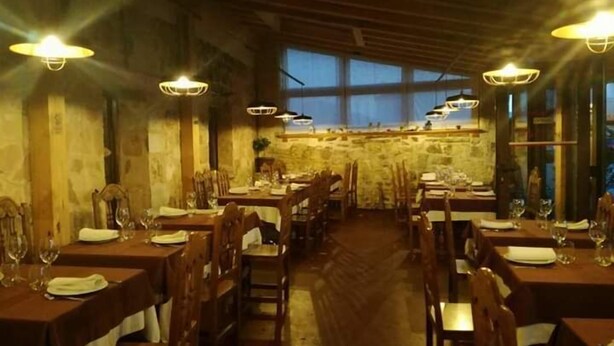 A restaurant with wooden tables and chairs, large windows, and hanging light fixtures. - Hostal la Cerca (Arcones)