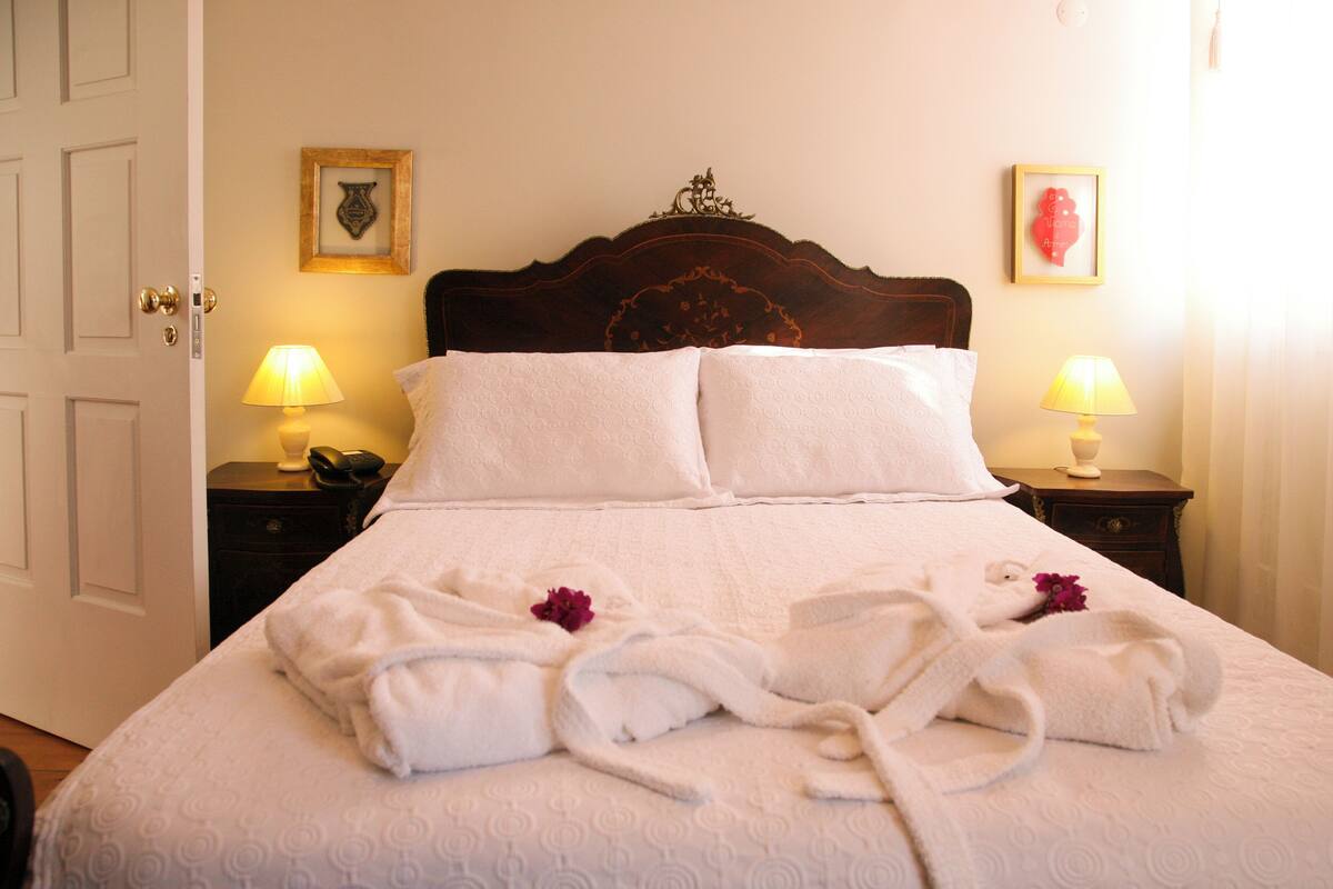 Una cama bien hecha con sábanas blancas y dos almohadas, dos mesitas de noche con lámparas, y un cuadro en la pared.