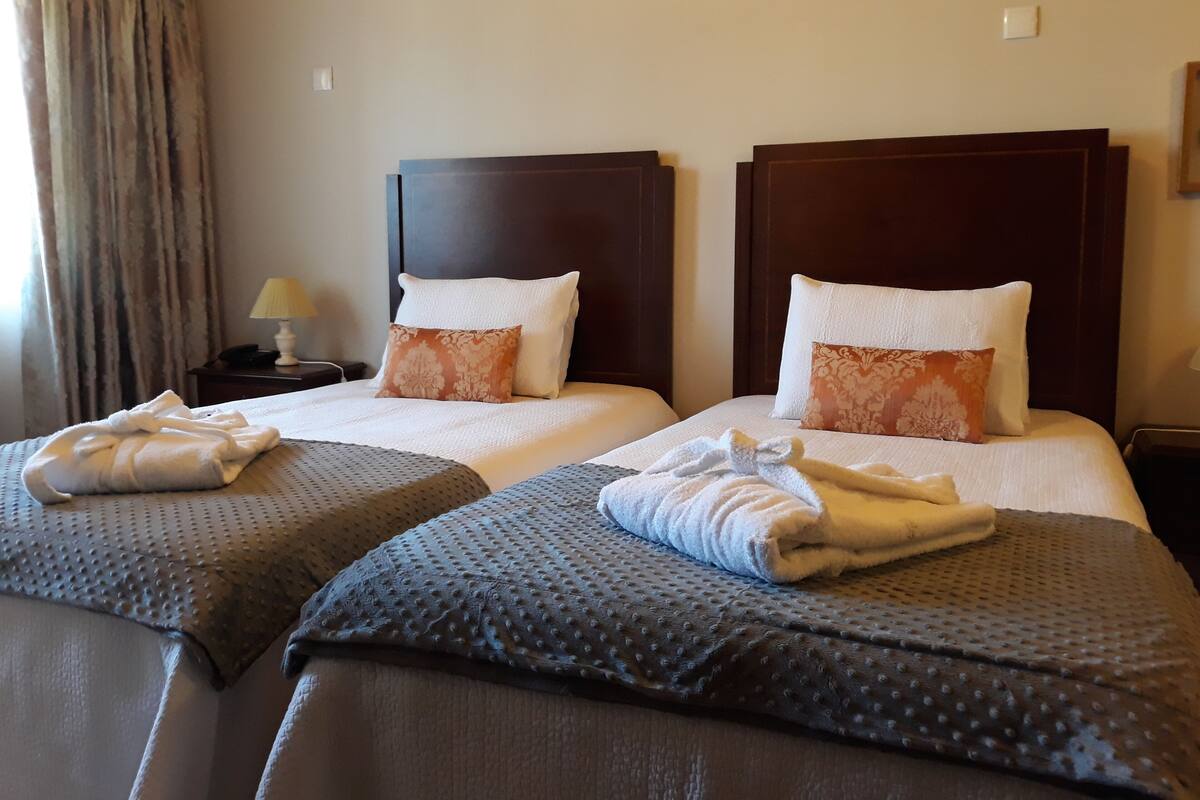 Habitación de hotel con dos camas, cada una con cabecero, almohadas y toallas dobladas.