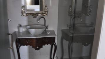 Une salle de bain avec un mur en marbre, un lavabo blanc, un miroir doté d’un cadre orné et une cabine de douche en verre.